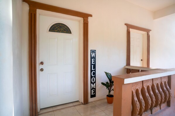 A reception area with a white door, a welcome sign, a potted plant, and a decorative wall feature. - Eleven30 Luxury Apartments  (Negril)
