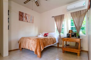 A neatly arranged bedroom with a bed, a bedside table, an air conditioner, and a window with curtains. - Eleven30 Luxury Apartments  (Negril)