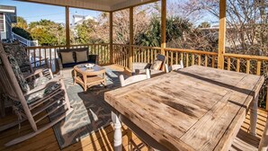 Ein überdachter Außenbereich mit Holztisch und -stühlen, einer gepolsterten Bank und Blick auf die umliegende Landschaft.