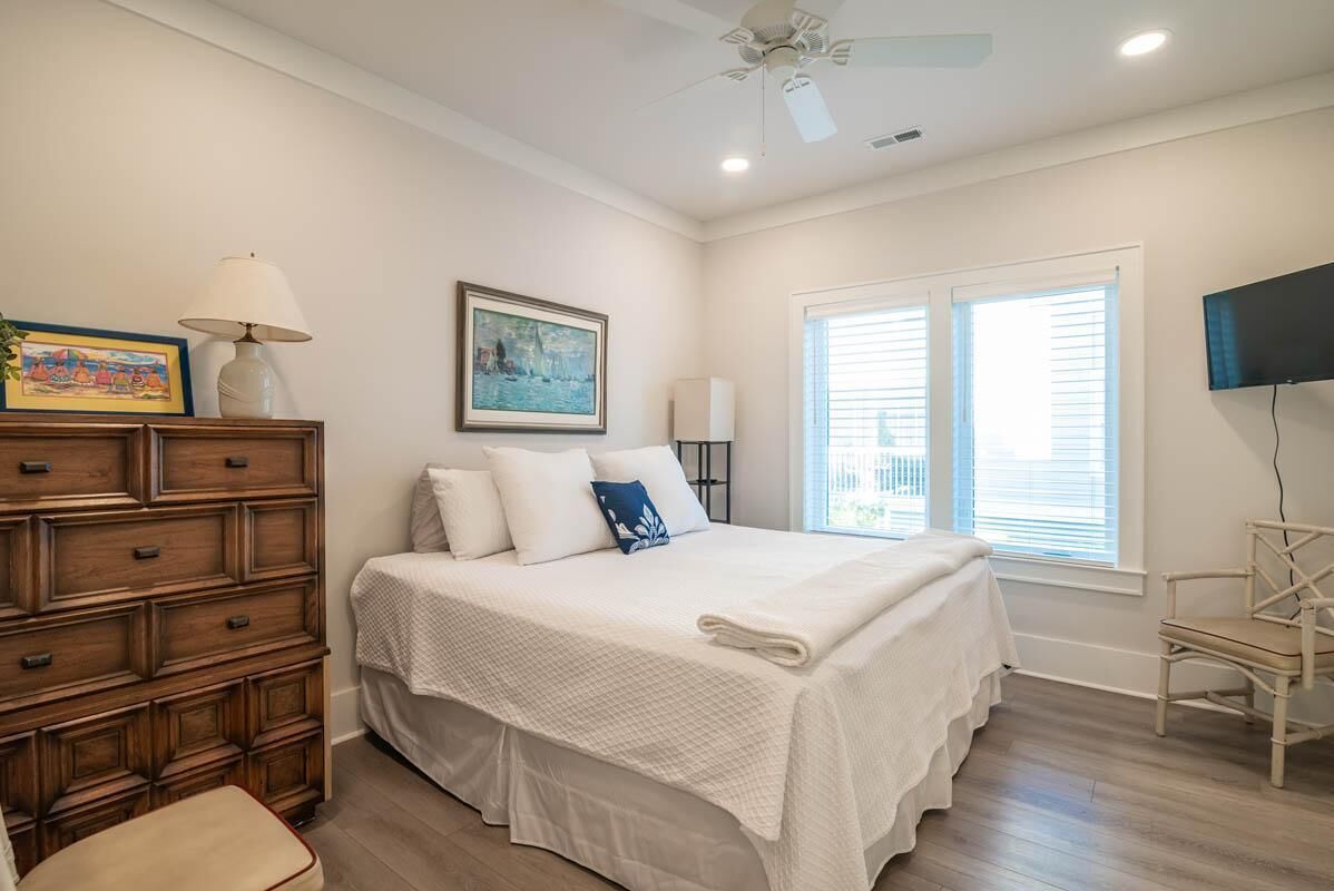 Quarto com uma cama grande, cômoda de madeira e ventilador de teto.