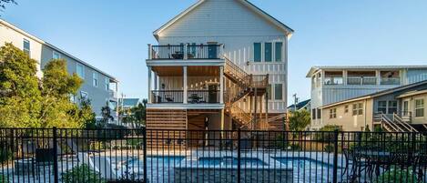 A two-story building with a balcony, a swimming pool, and a fenced area.