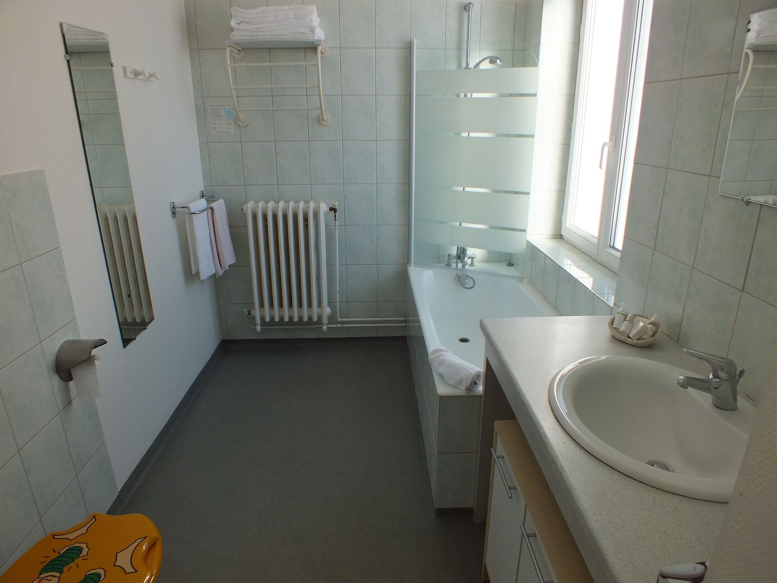 Un baño con bañera, lavamanos, espejo, toallero y radiador.