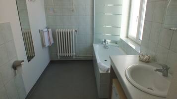 Un baño con bañera, lavamanos, espejo, toallero y radiador.