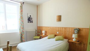 Habitación de hotel con una cama grande, dos lámparas de noche, cabecero de madera, radiador, una silla, una mesa y un teléfono.
