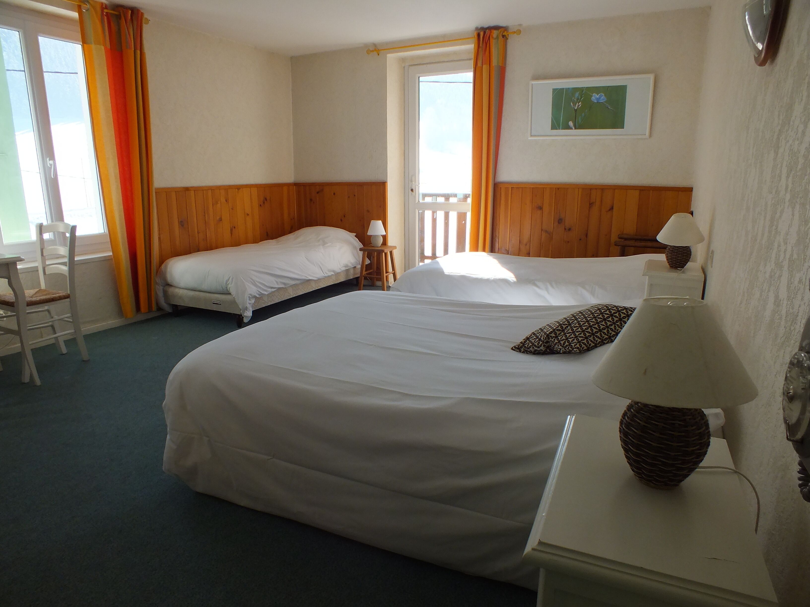 Ein Hotelzimmer mit zwei Betten, einem Sessel, einem Tisch, einer Lampe und einem Fenster mit Vorhängen.