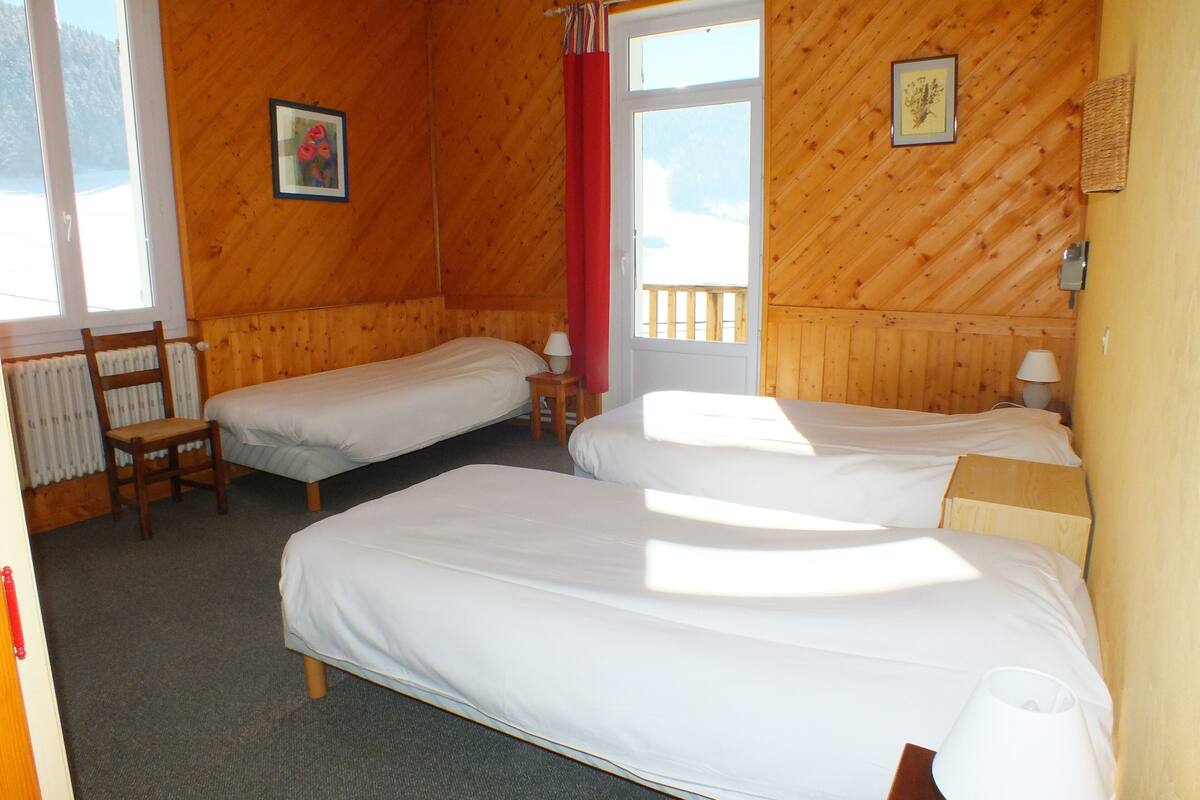 A room with two beds, wooden walls, a window, and a radiator.