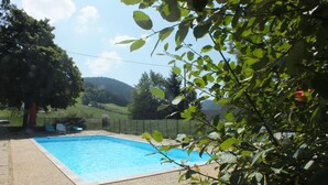 Una piscina rodeada de una valla, con vistas a colinas y árboles al fondo.