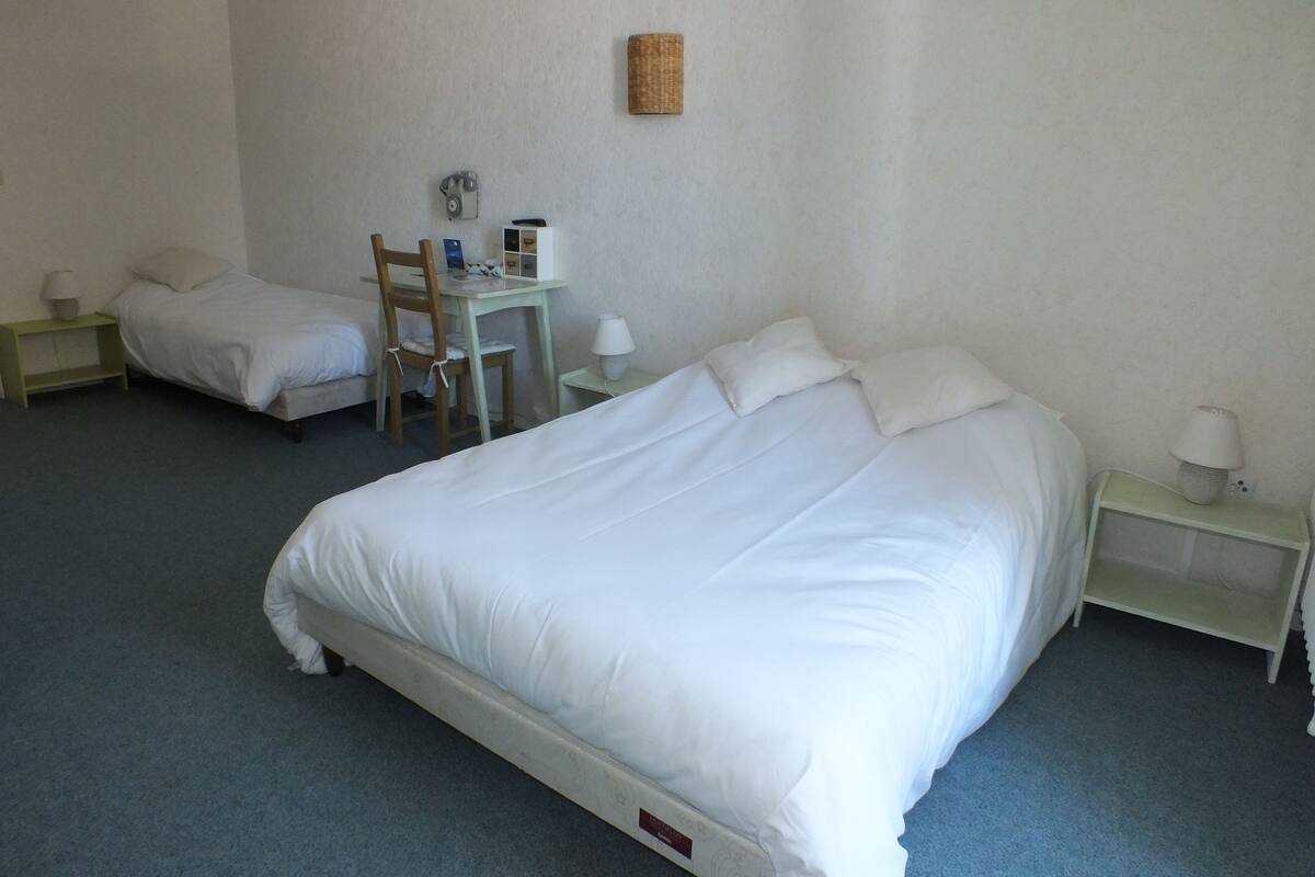 A hotel room with two single beds, a desk with a chair, and two bedside tables with lamps.