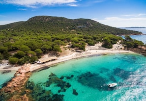 A coastal landscape with a beach, clear turquoise waters, and a mountainous backdrop.