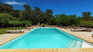 Une piscine rectangulaire bordée de pierres, entourée de chaises longues et d’un mur en pierre.