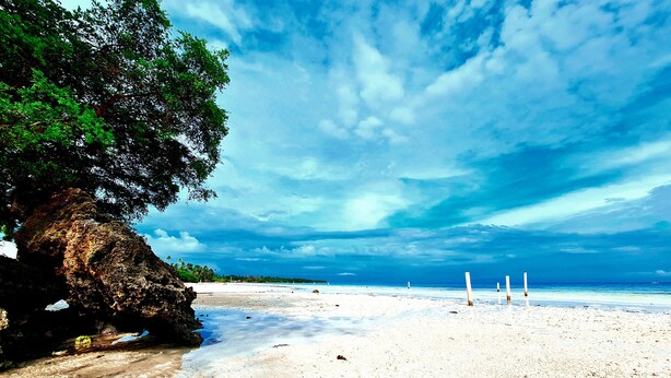 A beach with white sand, a large rock formation, and a clear blue sky. - La-Familia Guest House (Siquijor)