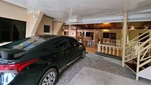 A black car parked in a covered parking area with a staircase leading to a dining area. - La-Familia Guest House (Siquijor)