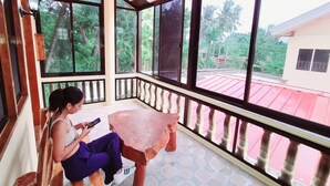 A person sitting on a bench inside a covered area with large windows, a tiled floor, and a railing. - La-Familia Guest House (Siquijor)