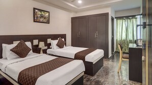 Quarto de hotel com duas camas, um ventilador de teto, um quadro na parede e uma mesa com uma cadeira.
