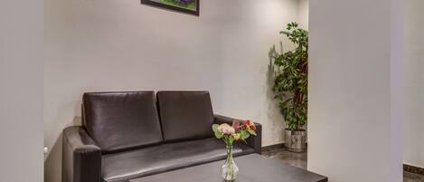 A modern hotel lobby with a leather sofa, a vase of flowers on a table, a large potted plant, and a framed picture on the wall.