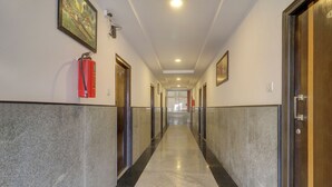 Um corredor com piso de mármore, portas em ambos os lados e um extintor de incêndio fixado na parede.