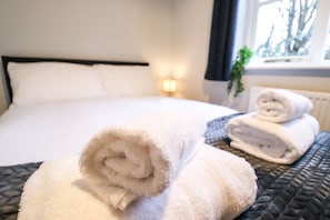 A neatly made bed with white linens and a rolled towel on the side.
