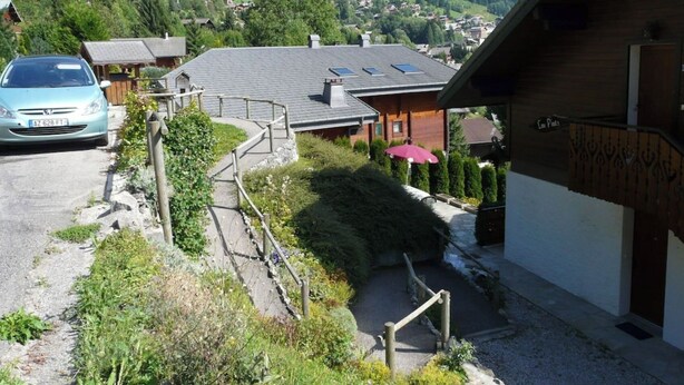 A rural setting with a house featuring a sloped roof, a visible garage, and a pathway leading to the entrance. - Châtel - Roitet : 3P apartment, quiet, breathtaking view in Chalet Lou P'nots  (Châtel)