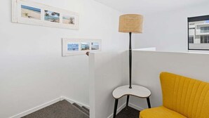 Een kamer met een witte muur, een gele stoel, een vloerlamp en twee ingekaderde foto's.