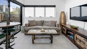 Een moderne woonkamer met een bank, salontafel, televisie en een eethoek met stoelen.