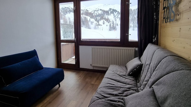 A room with a blue sofa, a grey sofa, and a view of a snowy mountain landscape through a sliding glass door.