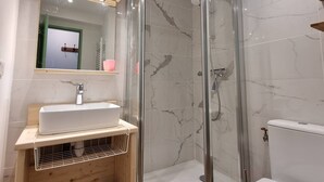 A modern bathroom with a glass-enclosed shower, a wooden vanity with a sink, and a mirror with lights.