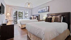A hotel room with two beds, a desk, a TV, and a large window with a view of trees. - Saint James Place 233A (Beaver Creek)