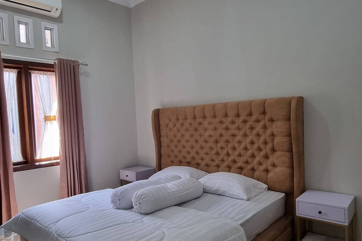 Un dormitorio ordenado con una cama grande, una mesita de noche y un equipo de aire acondicionado en la pared.