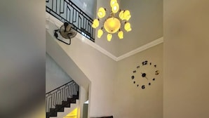Una sala de estar con un sofá modular, una mesa de centro, un reloj en la pared, una escalera con barandilla y un candelabro.