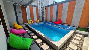Una piscina rectangular con borde de azulejos, rodeada por un deck con revestimiento de piedrecitas y cojines de colores.
