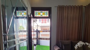 Un salón amplio con un gran ventanal que da a un balcón, un sofá marrón y una mesita con un jarrón de flores.