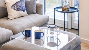 A modern living room with a sofa, a glass coffee table, and a side table with a candle and a container. - Sea view for 4 people, 2 en-suite bathrooms, balcony, directly on the beach (Prora (Binz))