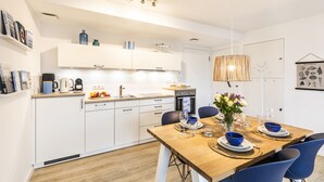 A modern kitchen with white cabinets, a wooden countertop, and a dining area with a wooden table set for four. - Sea view for 4 people, 2 en-suite bathrooms, balcony, directly on the beach (Prora (Binz))