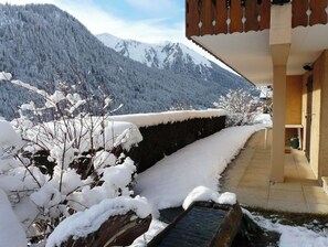 A snow-covered outdoor area with a wooden bench and a view of snow-capped mountains.