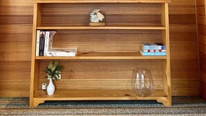 Een houten wand met een lijst met surfplanken en palmbomen, een plank met boeken en een vaas, en een thermostaat.