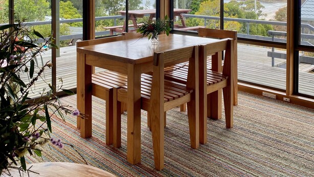 Een houten eettafel met stoelen in een kamer met grote ramen met uitzicht op een schilderachtig landschap.