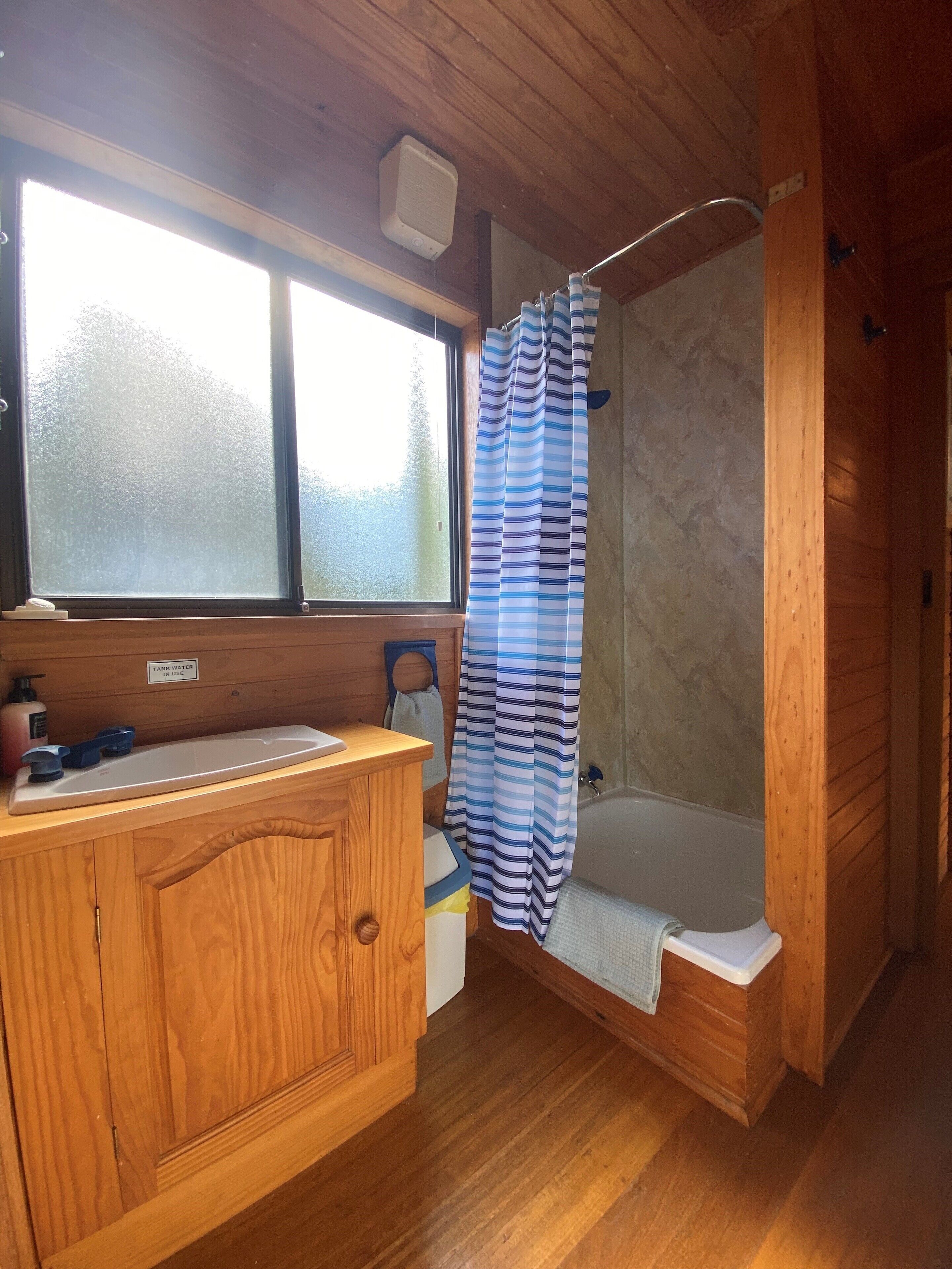 A wooden cabin bathroom with a shower, a window, and a sink with a towel rack.
