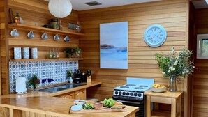 Een houten keuken met een centraal eiland, een fornuis en een klok aan de muur.
