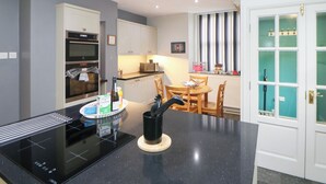 A modern kitchen with a built-in stove, oven, and microwave. There is a dining area with a table and chairs. - The Old Post Office (Matlock)