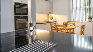 A modern kitchen with a black countertop, stainless steel appliances, and a dining area with wooden chairs and a table. - The Old Post Office (Matlock)