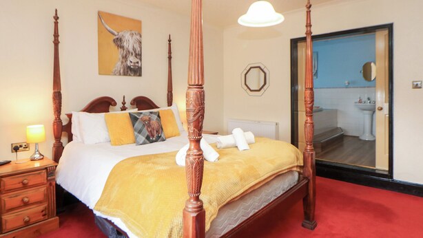 A four-poster bed with a yellow blanket, a bedside lamp, and a mirror in the room. - The Old Post Office (Matlock)