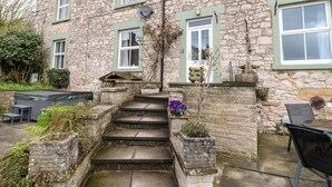 A stone house with a set of stone steps leading to a front door, surrounded by potted plants and a small outdoor seating area. - The Old Post Office (Matlock)