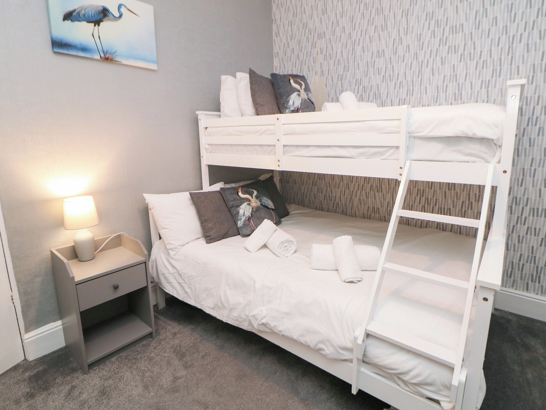 A bunk bed room with a nightstand, a lamp, and a wall-mounted picture.