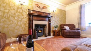A living room with a fireplace, a sofa, a table with a bottle of wine, and a decorative wall. - The Old Post Office (Matlock)