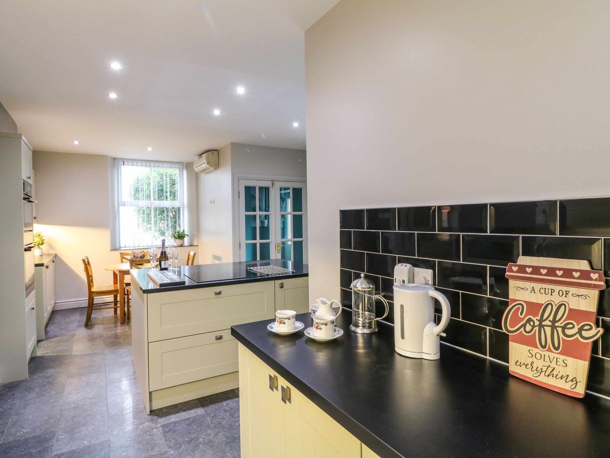 A modern kitchen with a black countertop, white cabinets, and a coffee sign.