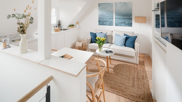 A modern, minimalist living room with a white sofa, a coffee table, and a view of the sea through large windows. - House Salz&Sand // Apartment Lüttje Tide (Norderney)