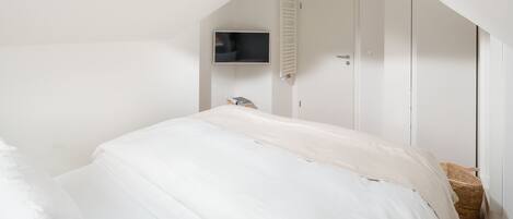 A bedroom with a bed, a television mounted on the wall, a door, and a small wicker basket.