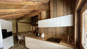 A compact kitchen with white cabinetry, a black stove, and a wooden ceiling. - Central 3-BR Apartment for 6 with WiFi, Parking & Spa Access (Les Carroz d'Arâches)