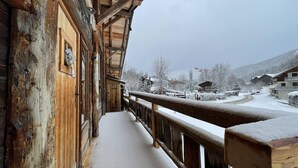 A wooden cabin with a balcony, snow-covered ground, and a view of a snowy village. - Central 3-BR Apartment for 6 with WiFi, Parking & Spa Access (Les Carroz d'Arâches)