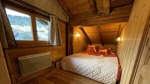 A cozy wooden cabin bedroom with a bed, a window with curtains, and a radiator. - Central 3-BR Apartment for 6 with WiFi, Parking & Spa Access (Les Carroz d'Arâches)